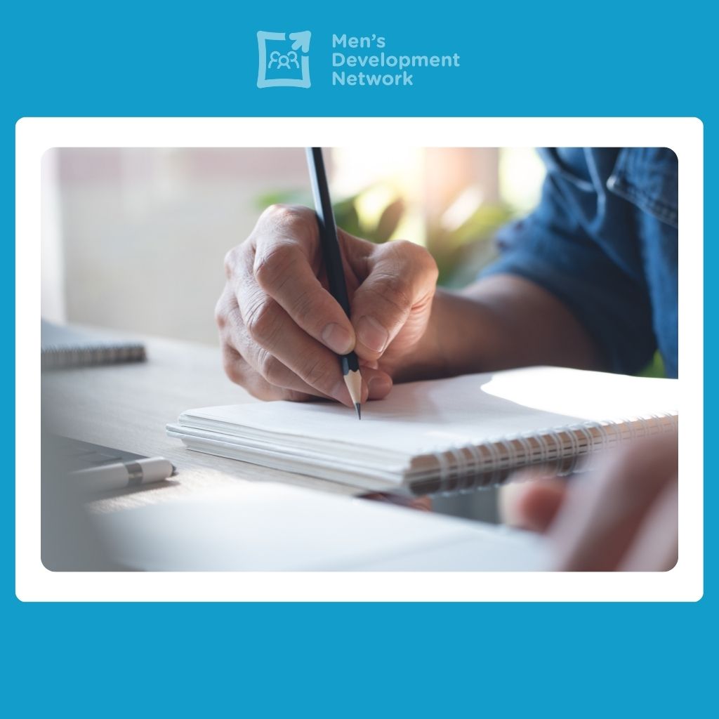 A person writing in a notebook, representing further learning and personal reflection through the Men’s Development Network’s masculinity resources.